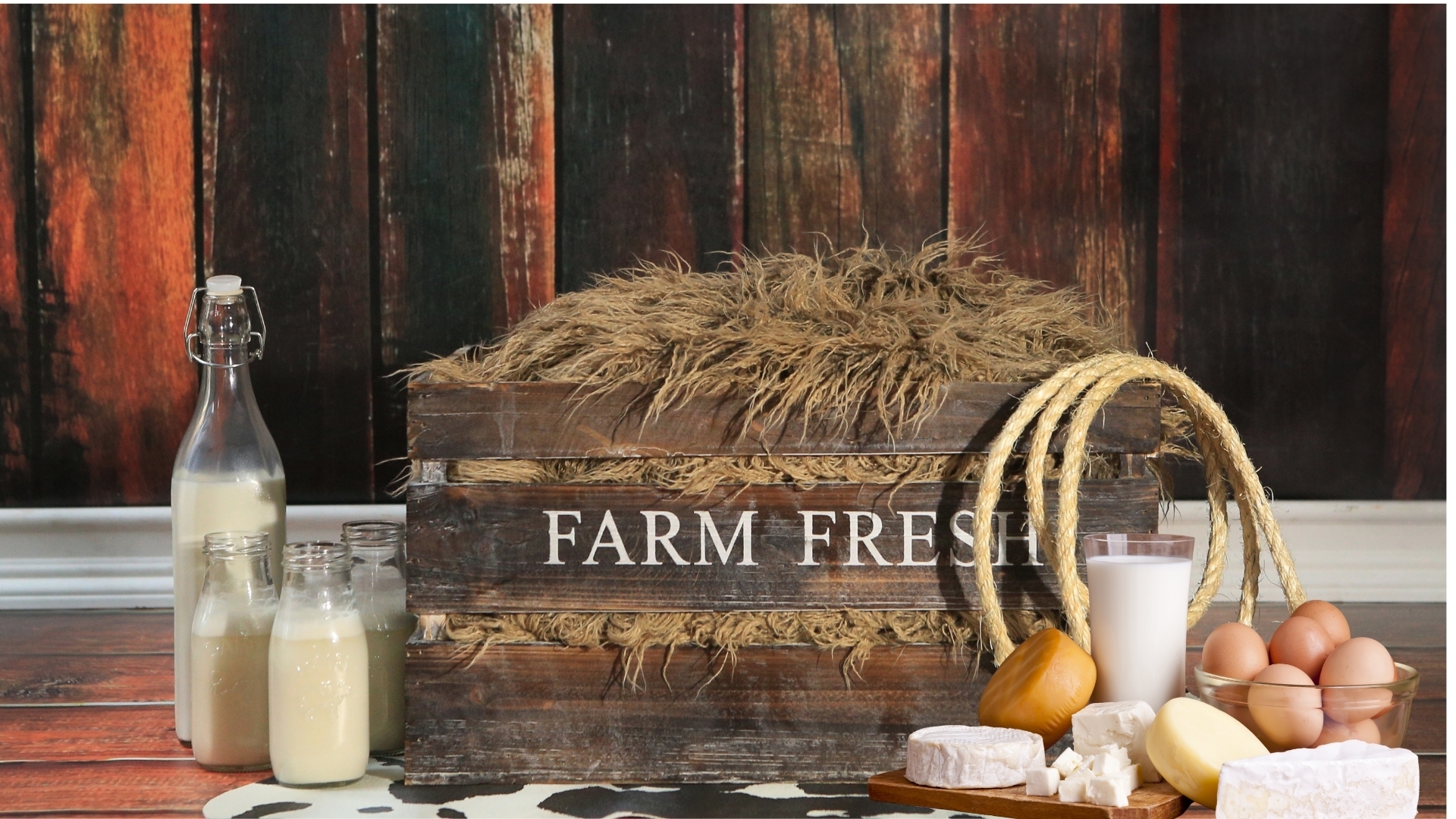 Productos de granja sobre una mesa de madera, con leche, quesos, mantequilla, huevos y una caja rústica, que simbolizan las pequeñas elecciones concretas que apoyan a los campesinos y refuerzan una alimentación más soberana.